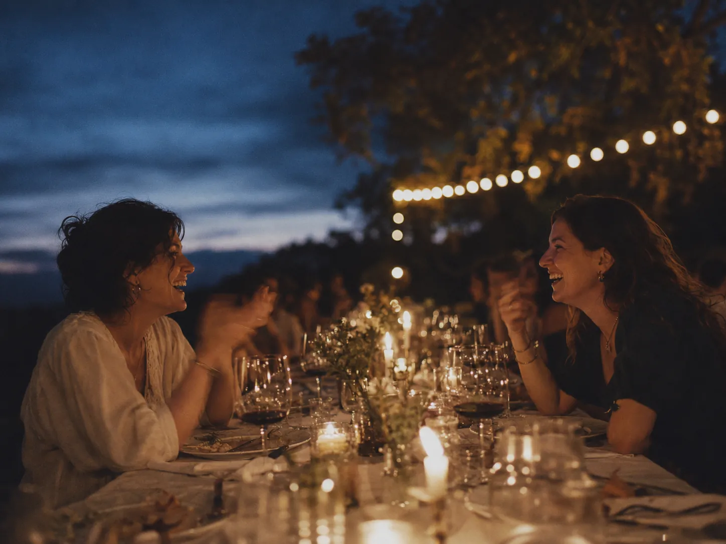 Friends laughing at candlelit outdoor dinner